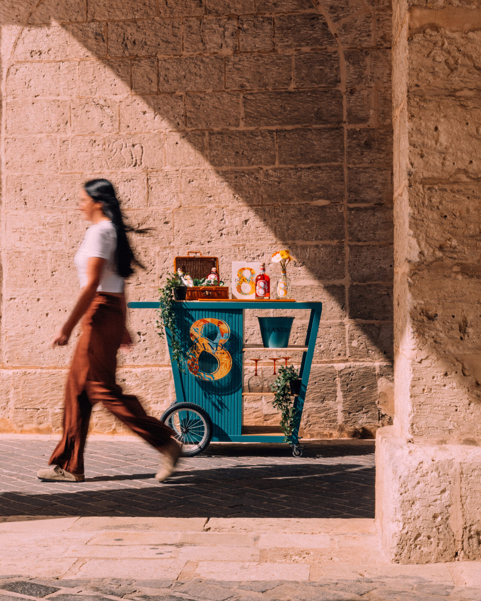 A woman walking past the Islands8 bar cart in a Maltese street